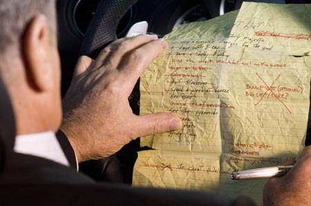 Links im Bild ein Fahrer, eine geknickte, handgeschriebene Liste liegt auf dem Lenkrad, die rechte Hand hält eine silbernen Stift.